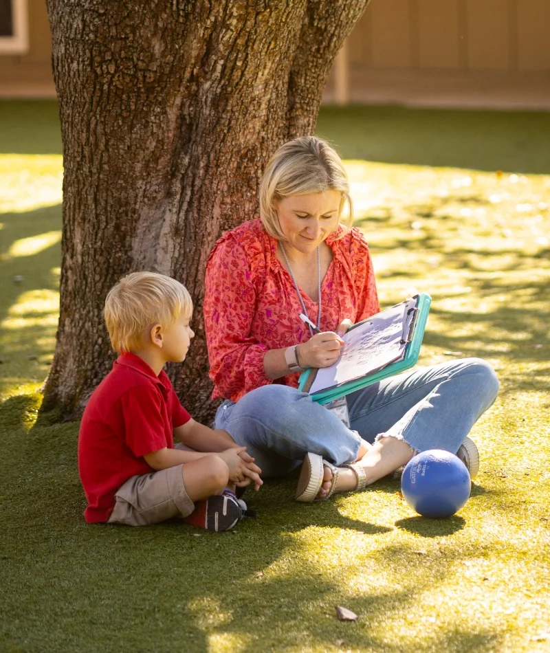 toddler student and teacher sitting under a tree
