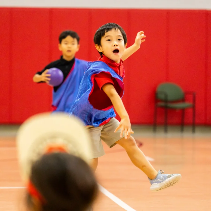 student in gymnasium with a blue jersey on throwing a ball